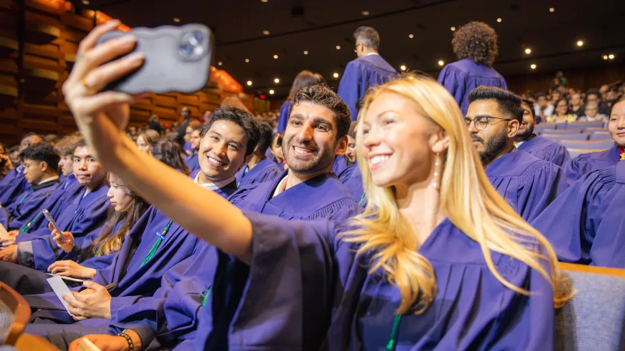 Seated students in their graduation gowns take a selfie together