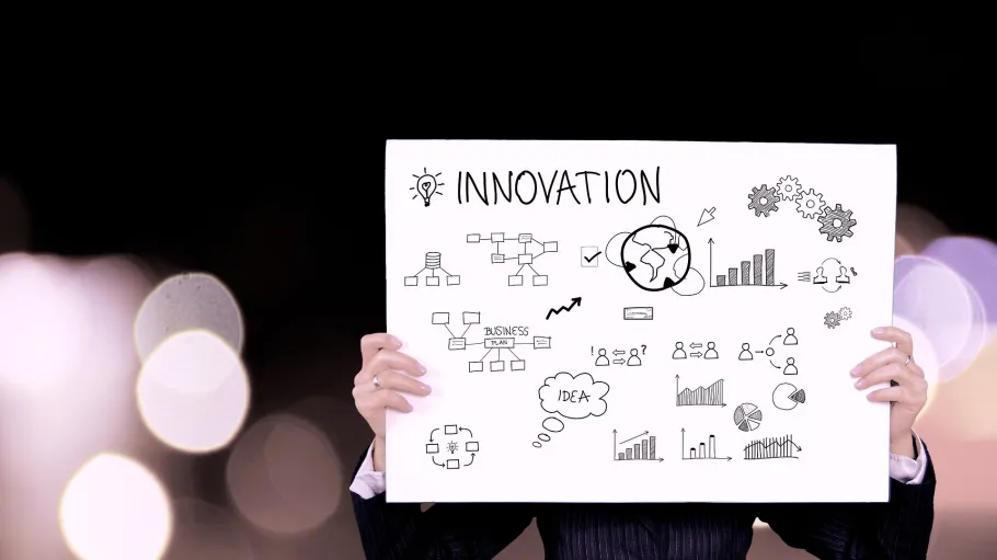 Person holding a poster with the word "Innovation" and sketches of ideas, charts, and gears.