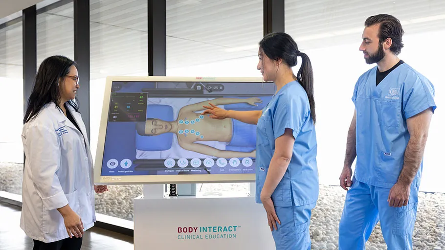 Two students stand beside a hi-tech screen as they talk to an instructor.