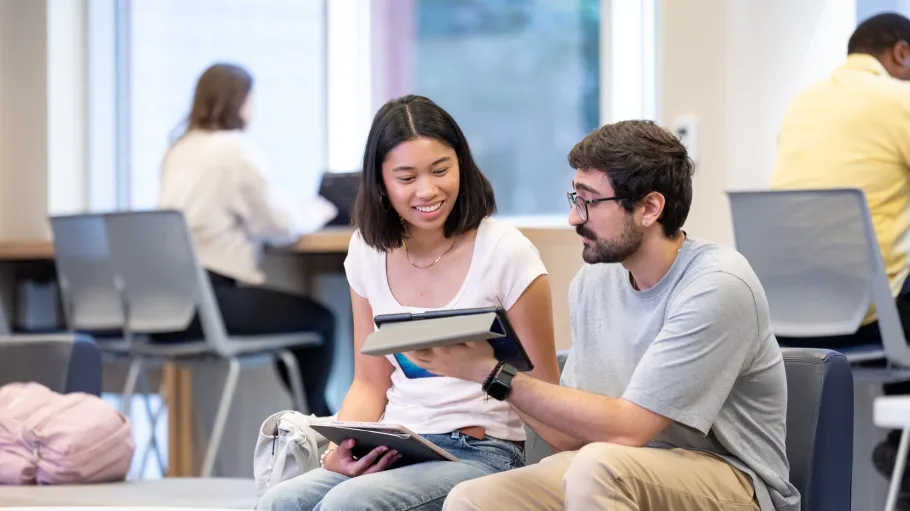 Two seated students look at a tablet