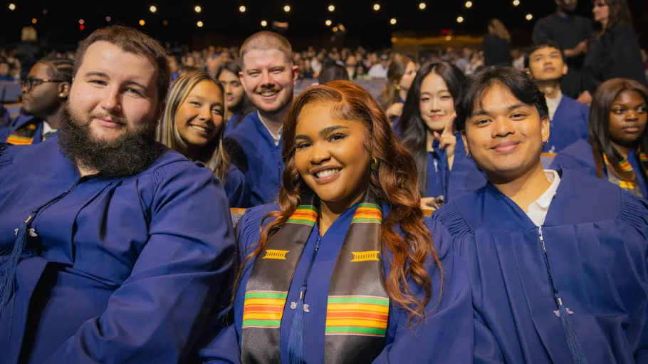 New grads seated in their robes at the 2026 convocation ceremonies smile for the camera.