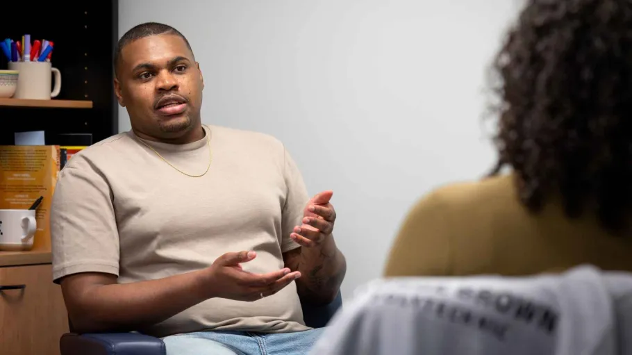 A student speaks with a counsellor, with the camera focused on the student. He's gesturing with his hands while he talks.