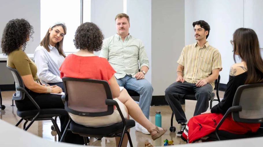 A group of students and counsellors sit in a circular formation, looking at each other.
