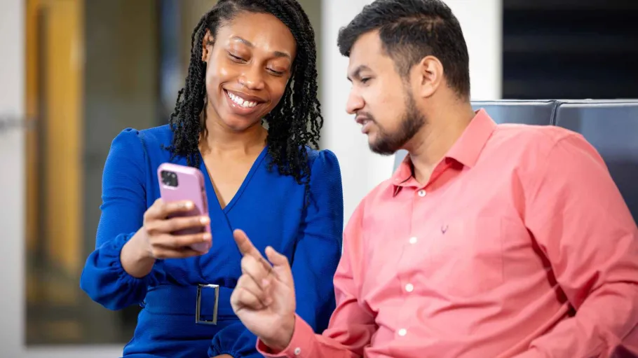 One student holds a phone while another student looks and points at it.