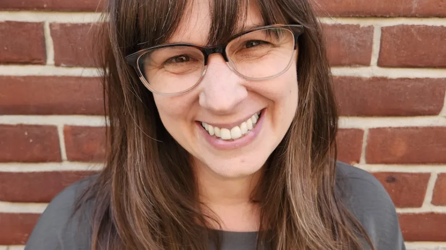 A woman with brown hair and glasses against a brick wall.