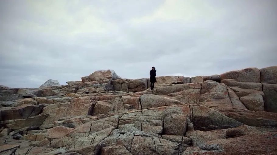 A landscape image of a person standing far away on some rocks.