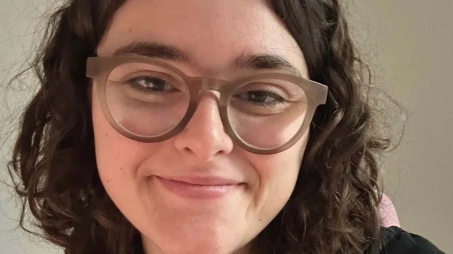 A woman with curly brown hair and glasses wearing a black shirt.