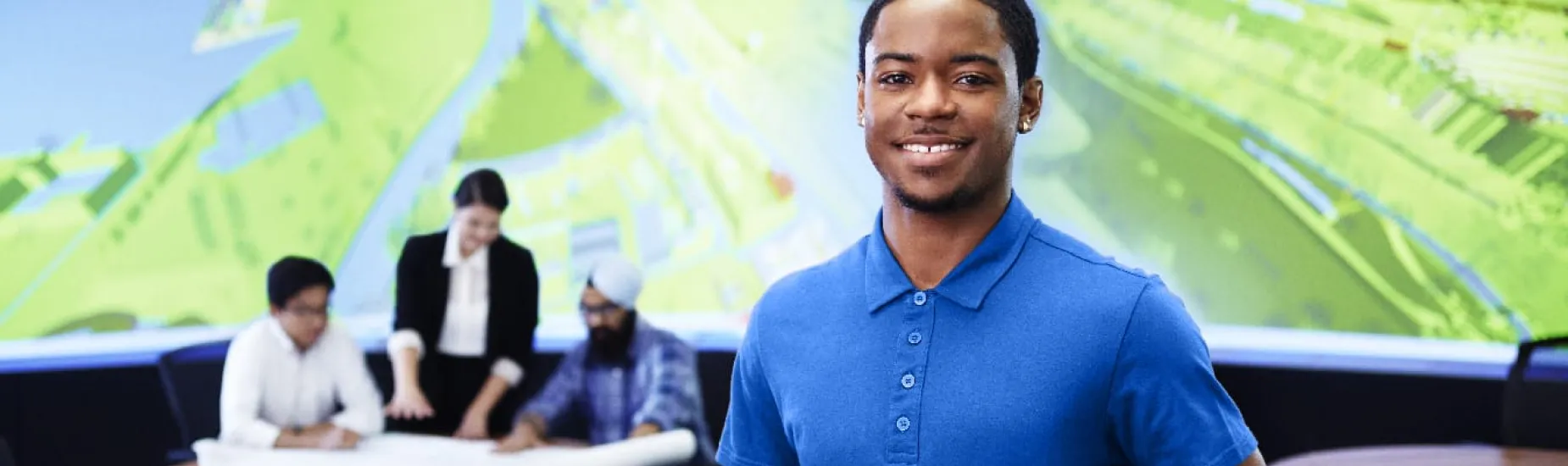 Male architecture student posing with folder in the BIM lab with a 3D model on the table beside him. 