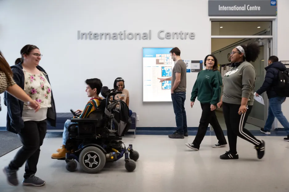 Students walking and one student driving an electric wheelchair in front of the International Centre at St. James Campus.