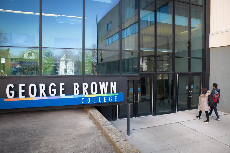A male and female student walking towards a Casa Loma campus entrance near a George Brown Polytechnic sign.