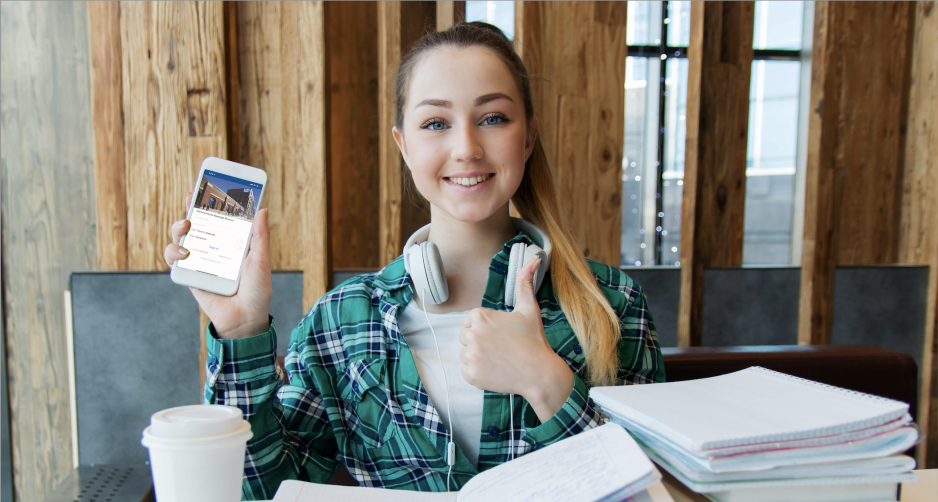 A student at a desk holding up a cellphone for the camera
