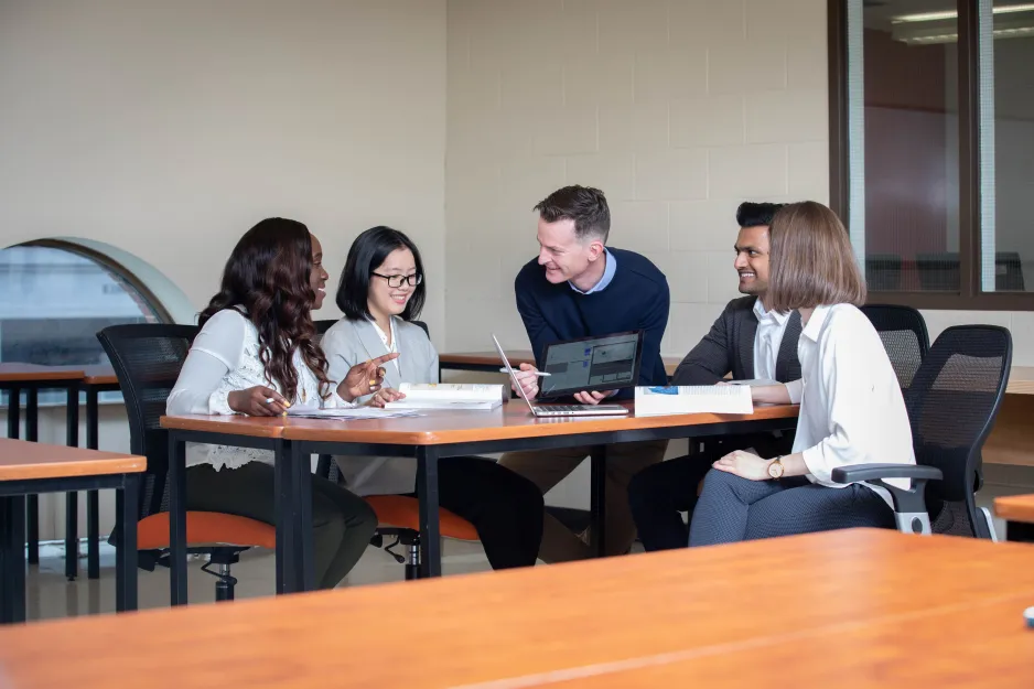 Business students sitting around a table with a professor teaching using a tablet.
