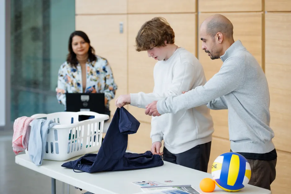 instructors helping a young man fold laundry