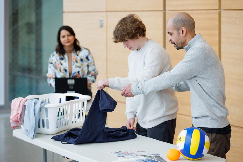 instructors helping a young man fold laundry