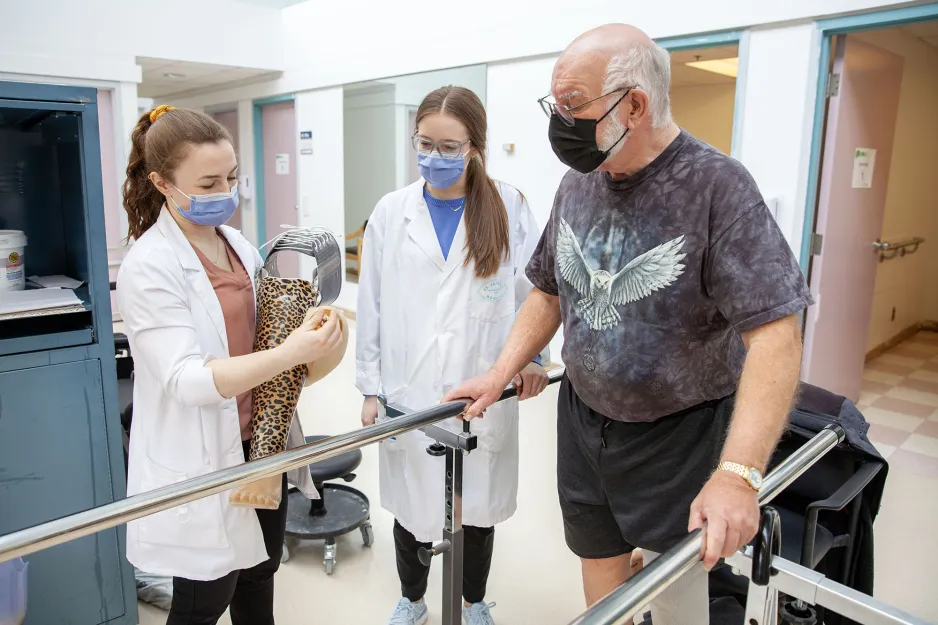 Two female Clinical Method in Orthotics/Prosthetic (S407) students provide an elderly male client with instructions about his new prosthetic limb.