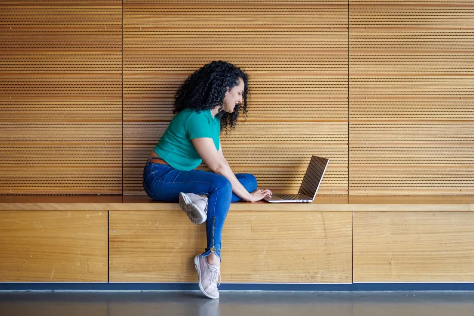 A student sits on a bench, using a laptop.