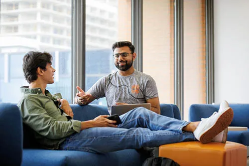 Two seated students chat while on campus.