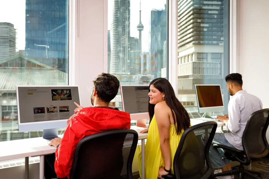 3 students in a computer lab with cityscape in the foreground.