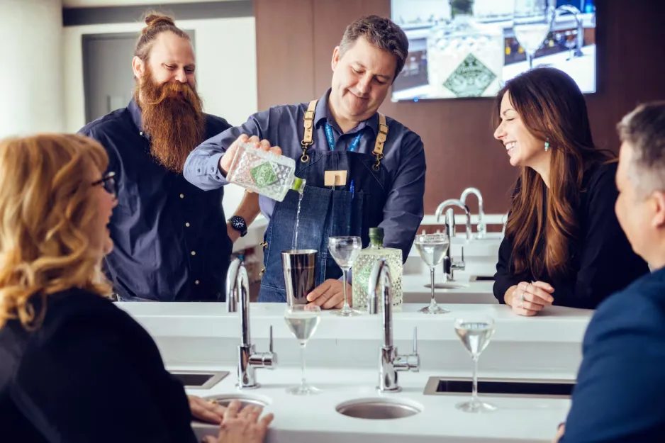A group of people watch as a person pours a drink from a cocktail shaker