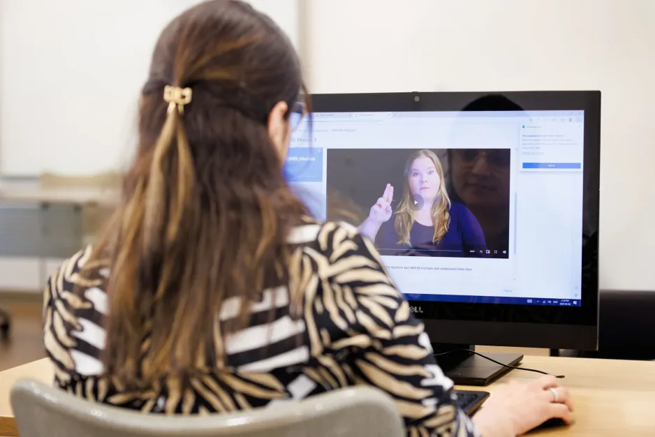 A woman looks at an American Sign Language training video on a screen