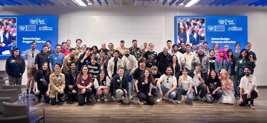 A group of game design alumni pose at the School of Design in a brightly lit room