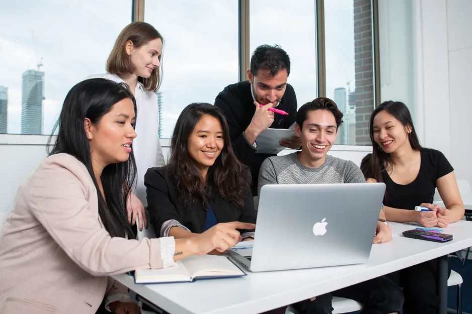 A group of students collaborate on a group assignment looking at a laptop together