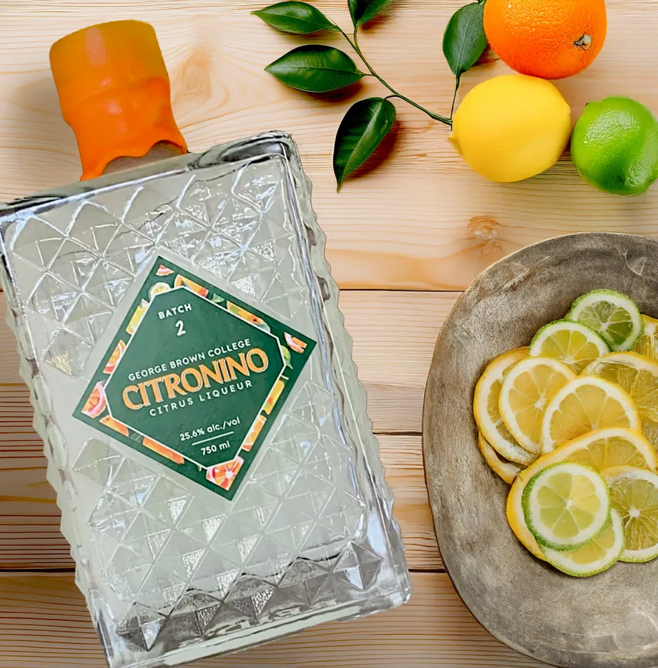 A glass Citronino 2.0 bottle on its side next to sliced citrus fruit