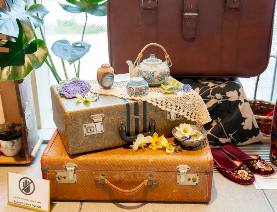 Suitcases stacked on top of each other with traditional shoes next to it, and a tea cup set on top.