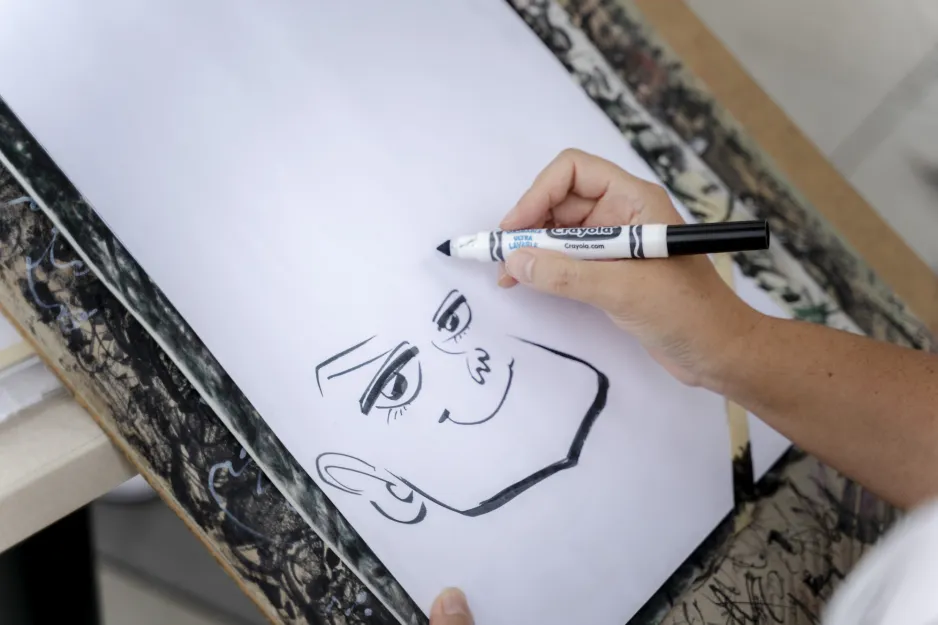 A caricature artist draws a visitor's face using a marker. 