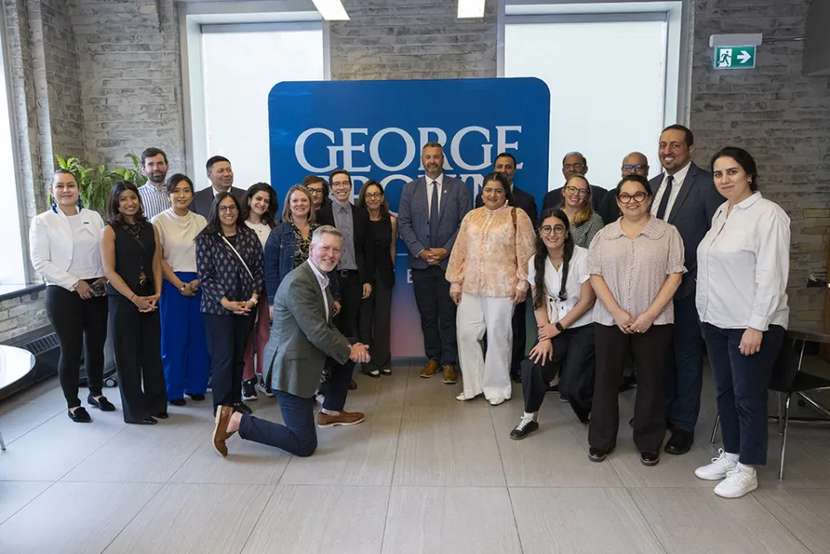 ReNEW alumni, staff and George Brown Polytechnic representatives gather for a group photo in front of a George Brown sign.
