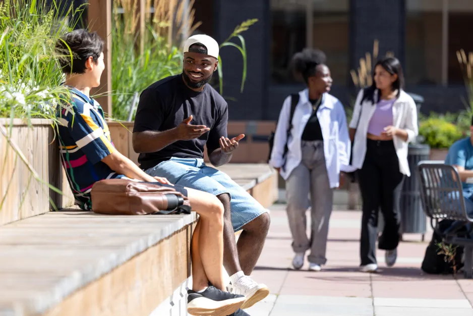 Two students seated on the St. James patio chat on a sunny day.