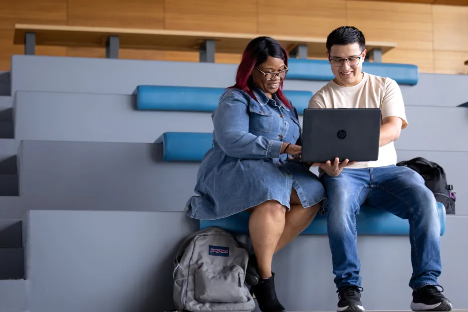 Two students are seated in a learning landscape looking at a laptop.