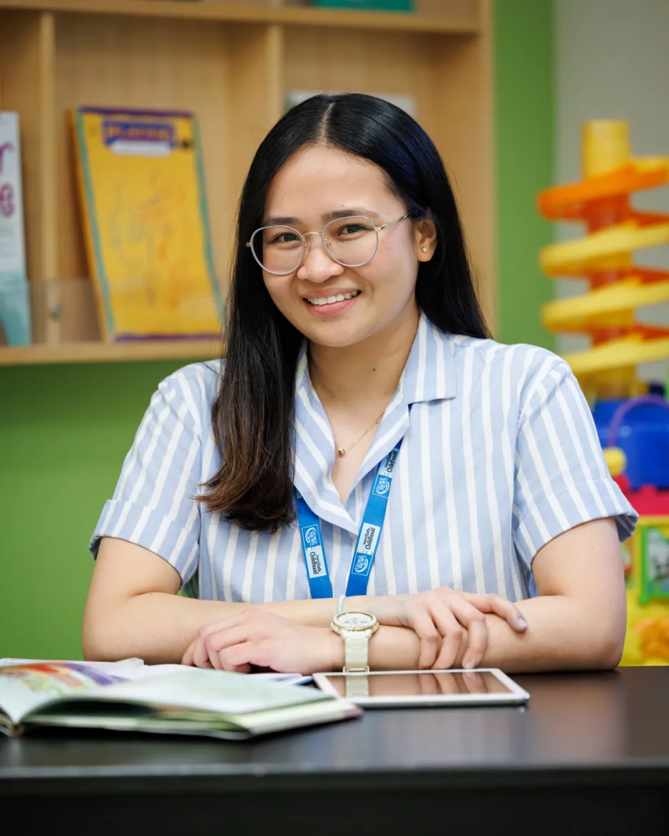 An Early Childhood student is seated at a table with toys and learning aids around her in a child care space.