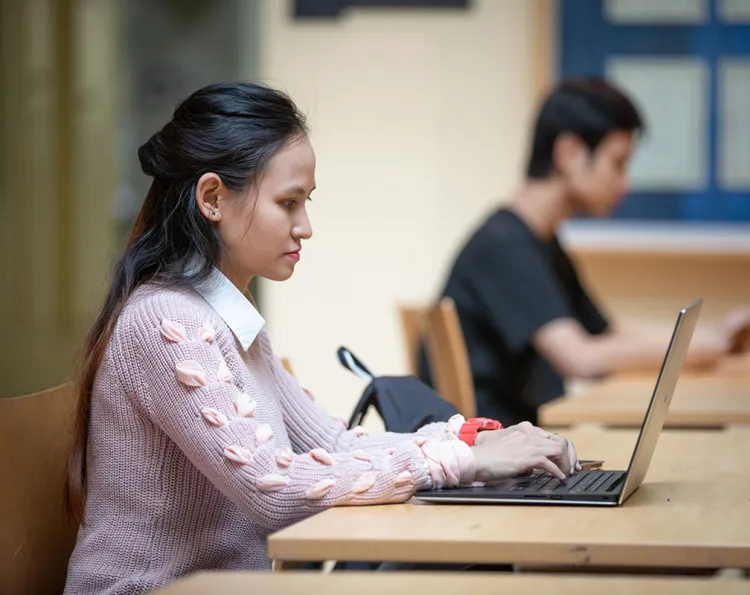 Female student using a laptop with another student in background