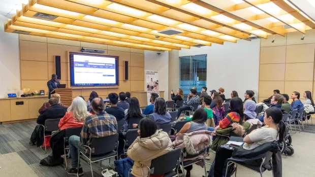 a picture of a speaker with a crowd sitting and watching the speaker