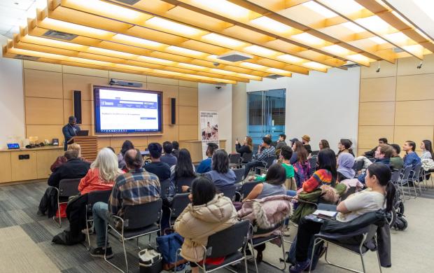 a picture of a speaker with a crowd sitting and watching the speaker