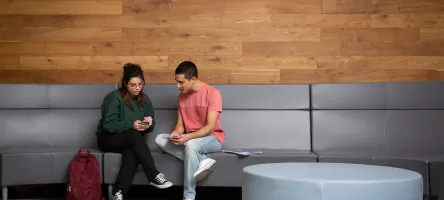 2 students sitting on a bench looking at a phone
