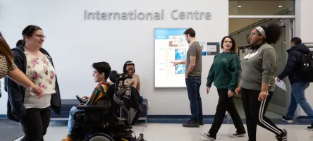 Students walking and one student driving an electric wheelchair in front of the International Centre at St. James Campus. 