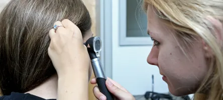 A female hearing specialist is working with a female patient where the specialist is using her equipment to observe the patient's inner ear canal.