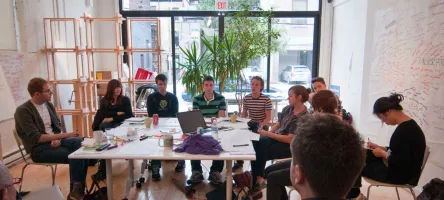 People in a meeting sitting around a table with computers and notebooks.