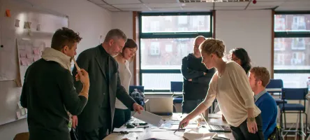 A group of people in a meeting looking at information on a table.