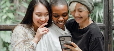 Three female students huddle around an outstretched cellphone.