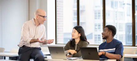 A Business professor speaks to two students in a classroom