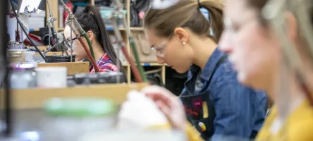 Students work behind jewellery benches with lights and equipment surrounding them