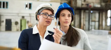 women students on construction site with blueprint