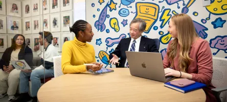 3 people sitting around a table discussing Items on a laptop.
