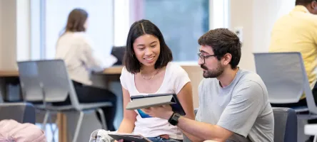 Two seated students look at a tablet