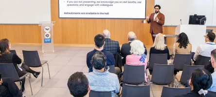 A speaker at the AI Centre of Excellence stands before and audience, giving a speech.