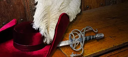 Period hat and sword lain across a wooden bench.