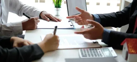 A close up of interviewers and interviewee's hands during a job interview. On the table is a laptop, papers, and calculator.